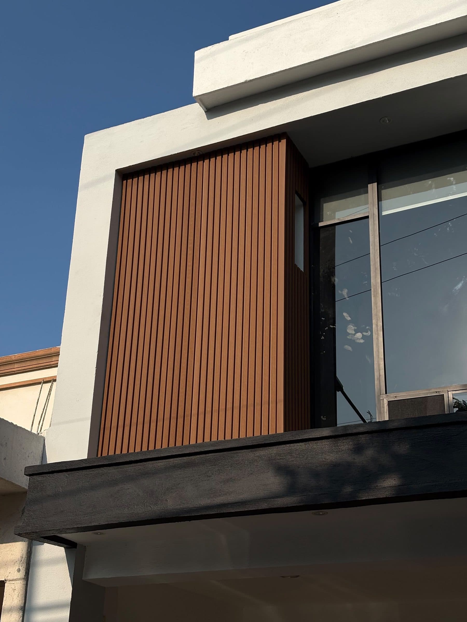 Fachada moderna con lambrín WPC vertical color teka instalado por Decktek