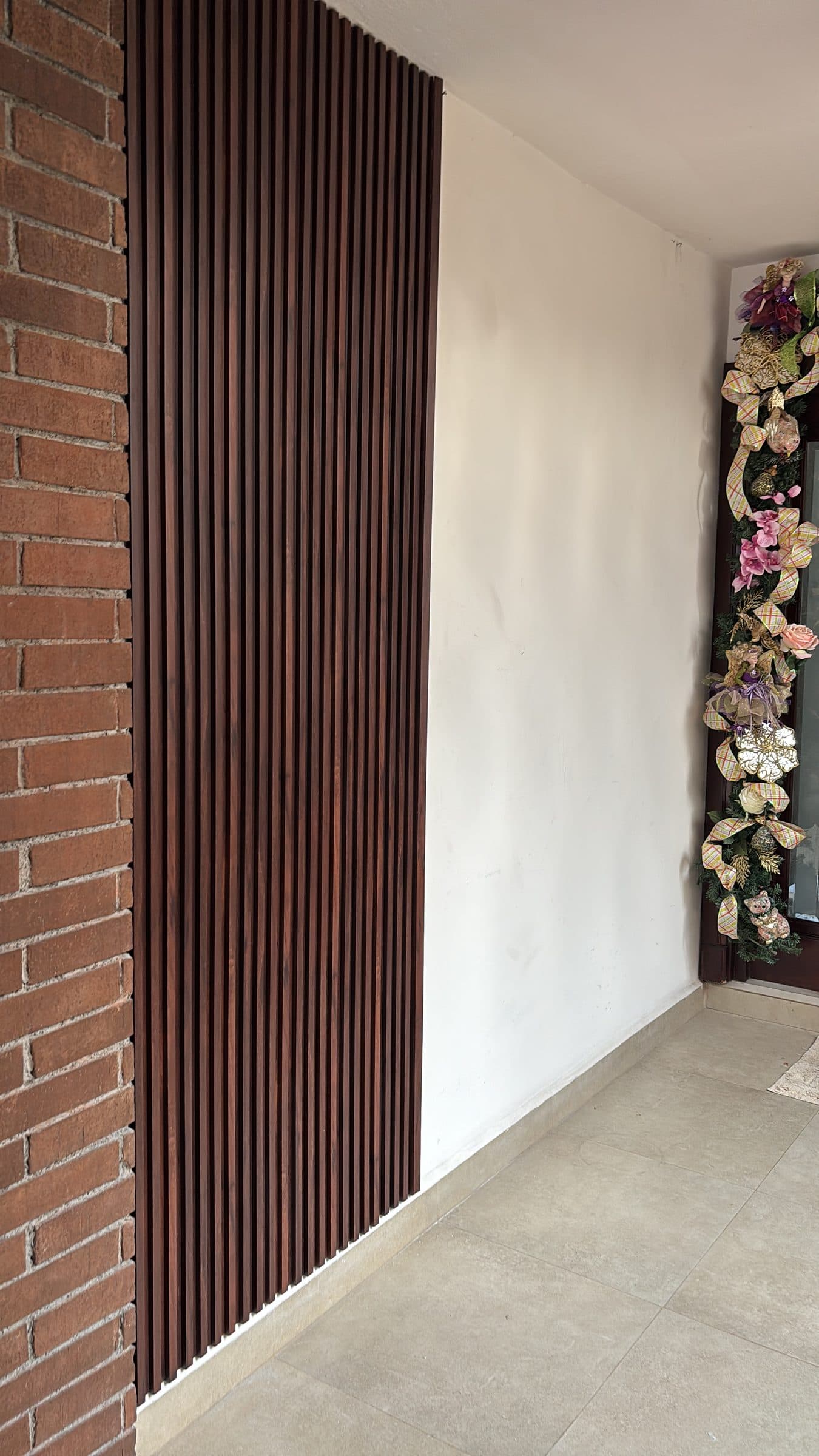 Acceso residencial con muro de lambrín WPC junto a ladrillo aparente